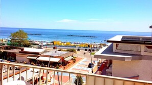 A coastal town with a view of the sea, buildings with balconies, and a paved area with shops.