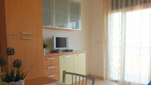 A room with a wooden cabinet, a television on top, a small table with a chair, and a window with curtains.