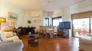 Ein geräumiges Wohnzimmer mit Fernseher, Essbereich und Balkon mit Sitzgelegenheit.