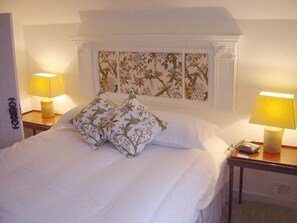 Un lit bien fait, avec du linge de lit blanc et deux coussins décoratifs, flanqué de deux tables de chevet sur lesquelles sont posées des lampes.
