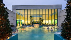 Un hotel moderno con una amplia piscina interior, rodeado de palmeras y fachada de vidrio.