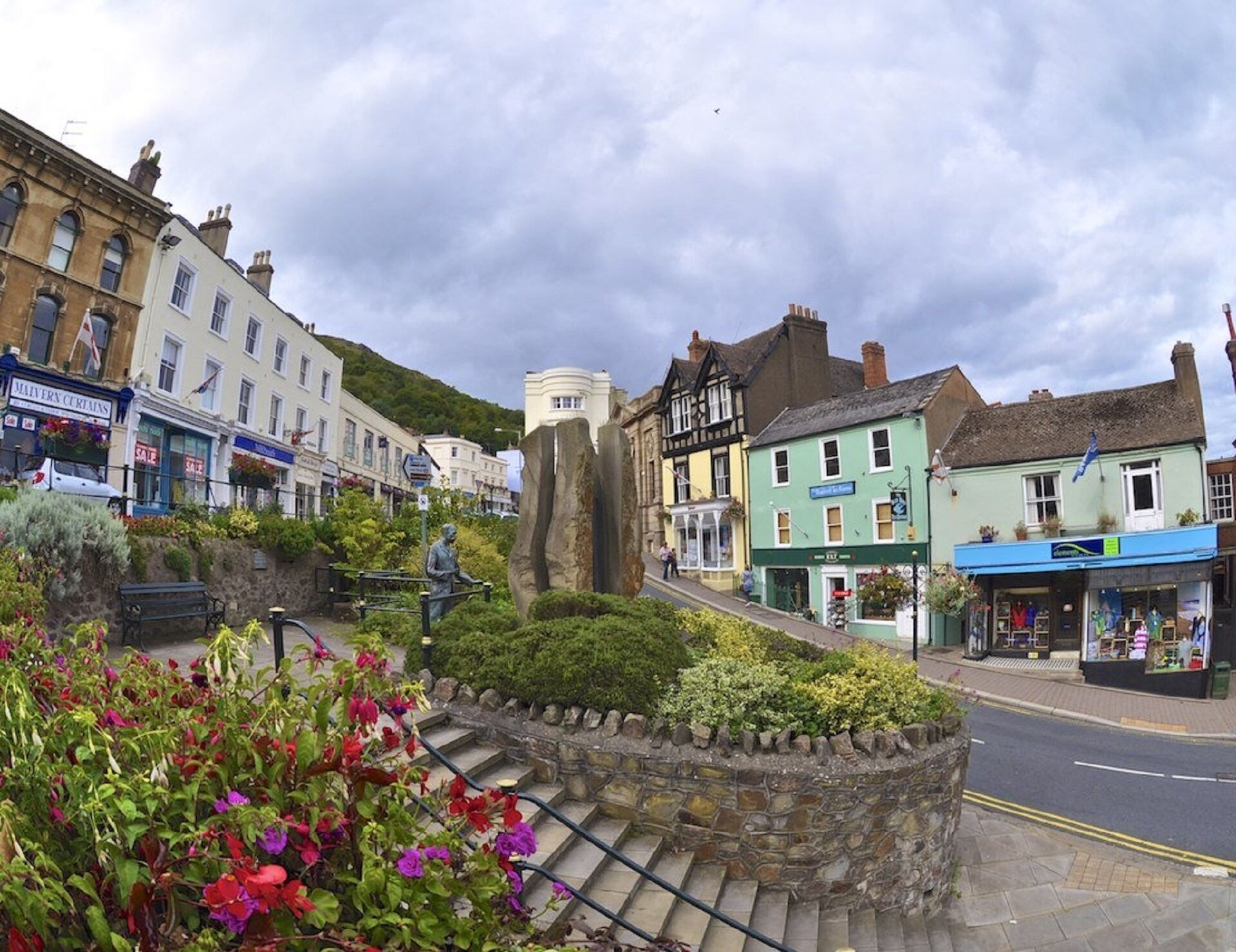 Une place de ville avec un monument en pierre, des boutiques et un escalier menant à une colline.