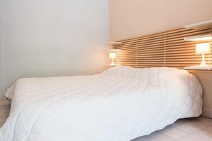 A neatly made bed with a white duvet, a wooden slatted headboard, and two bedside lamps.
