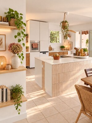 A modern kitchen with a central island, white cabinetry, and various plants.