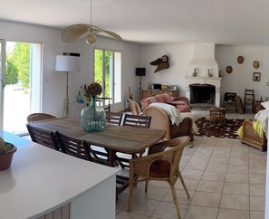 Un vaste espace de vie comprenant une table à manger, des meubles en osier, une cheminée et un ventilateur de plafond.