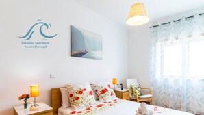 Een keurig opgemaakt slaapkamer met een bed, nachtkastjes, een lamp, een stoel en een raam met gordijnen.