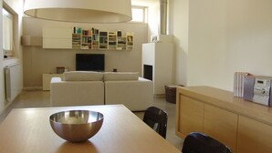 A modern living room with a sofa, a dining table with a metal bowl, a TV, and a bookshelf.
