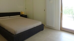 A bedroom with a bed, a nightstand, a lamp, and a sliding door to a balcony.