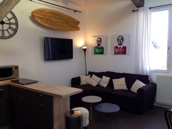 A modern living room with a sofa, a small table, a television, and a wooden surfboard on the wall.