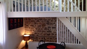 A dining area with a stone wall, a table with chairs, a lamp, and a staircase with white railings. - 2 ROOMS + MEZZANINE. All Biarritz on foot.  (Biarritz)