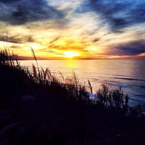 A sunset over a body of water with grass in the foreground.