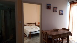 A bedroom with a bed, a table with a bowl, and a shower area. - Katerina Apartments ,( 1 ) One-Bedroom Apartment with Balcony (Kalamata)