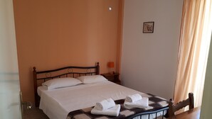 A neatly made bed with white linens, a checkered blanket, and folded towels on a metal frame bed in a room with peach walls. - Katerina Apartments ,( 1 ) One-Bedroom Apartment with Balcony (Kalamata)