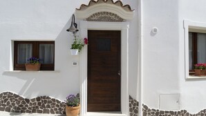 A house with a wooden door, a small window with a curtain, and a potted plant on the ground. - "Loft Costera" In the heart of the historic center of Orosei (Orosei, Nuoro)