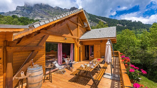 Eine Holzhütte mit einer Terrasse, Sitzgelegenheiten im Freien und Blick auf die Berge.