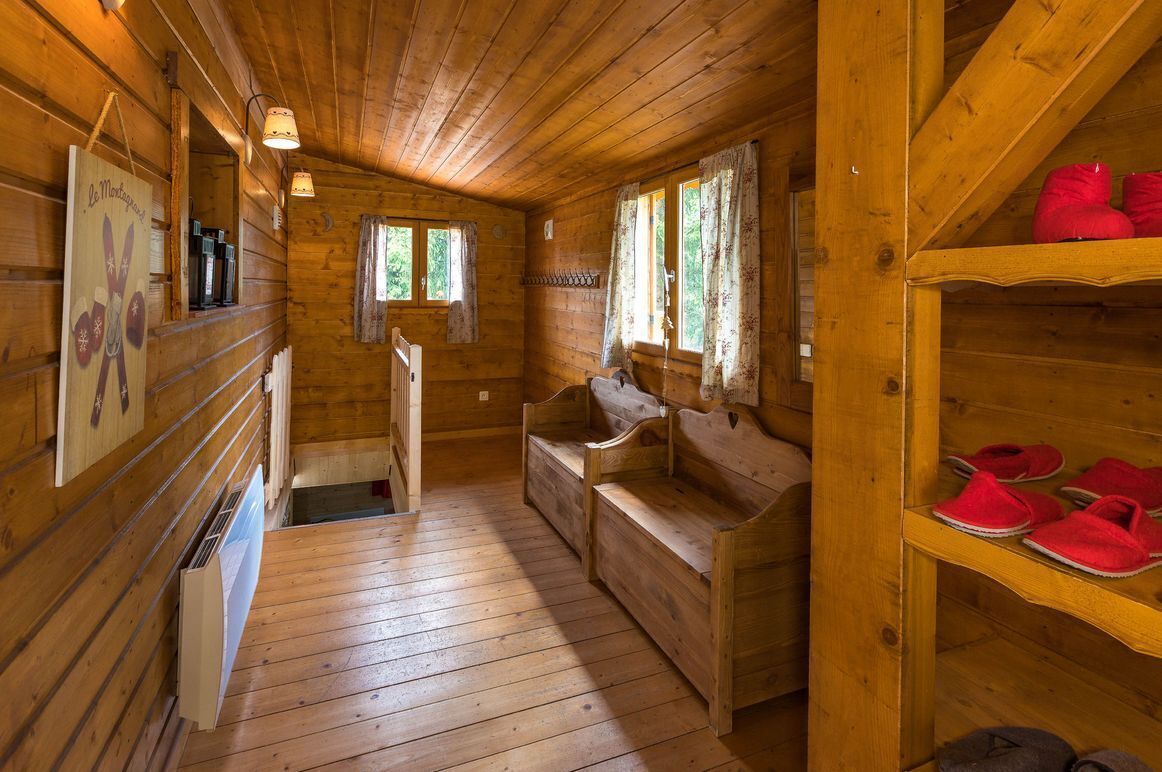 A wooden cabin interior with a wooden bench, a shelf with red slippers, and a radiator.