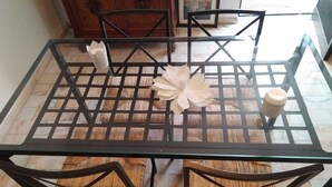A glass-top dining table with a woven chair design, a decorative white flower centerpiece, and a candle on the table. - Villa au Bord de Mer (Fontanelas)