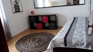 A bedroom with a bed, a large mirror, a dresser with red drawers, a patterned rug, and a wall-mounted artwork. - Villa au Bord de Mer (Fontanelas)