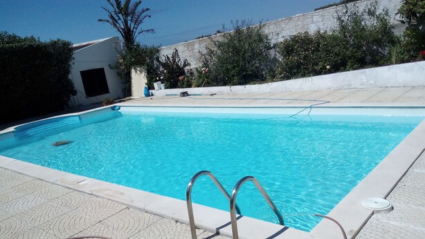 A swimming pool with clear blue water, a metal ladder, and a tiled deck. - Villa au Bord de Mer (Fontanelas)
