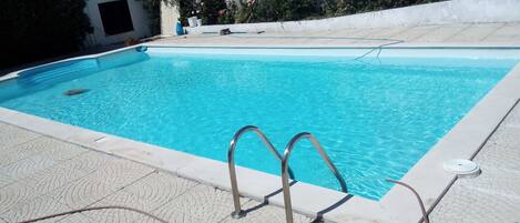 A swimming pool with clear blue water, a metal ladder, and a tiled deck.