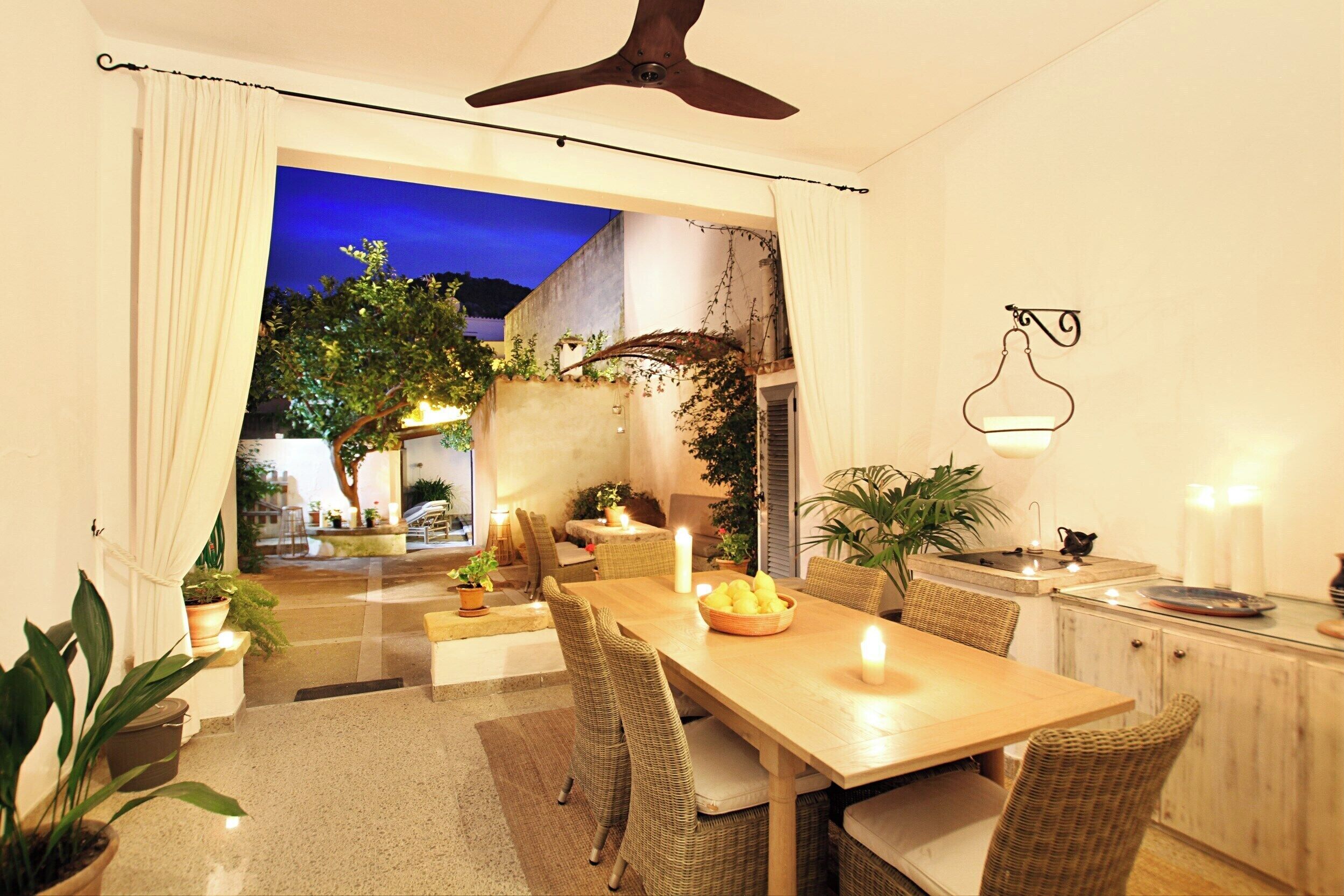 A dining area with a wooden table, wicker chairs, and potted plants.