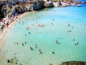 Ein Strand mit klarem Wasser und Menschen, die schwimmen und sonnenbaden.