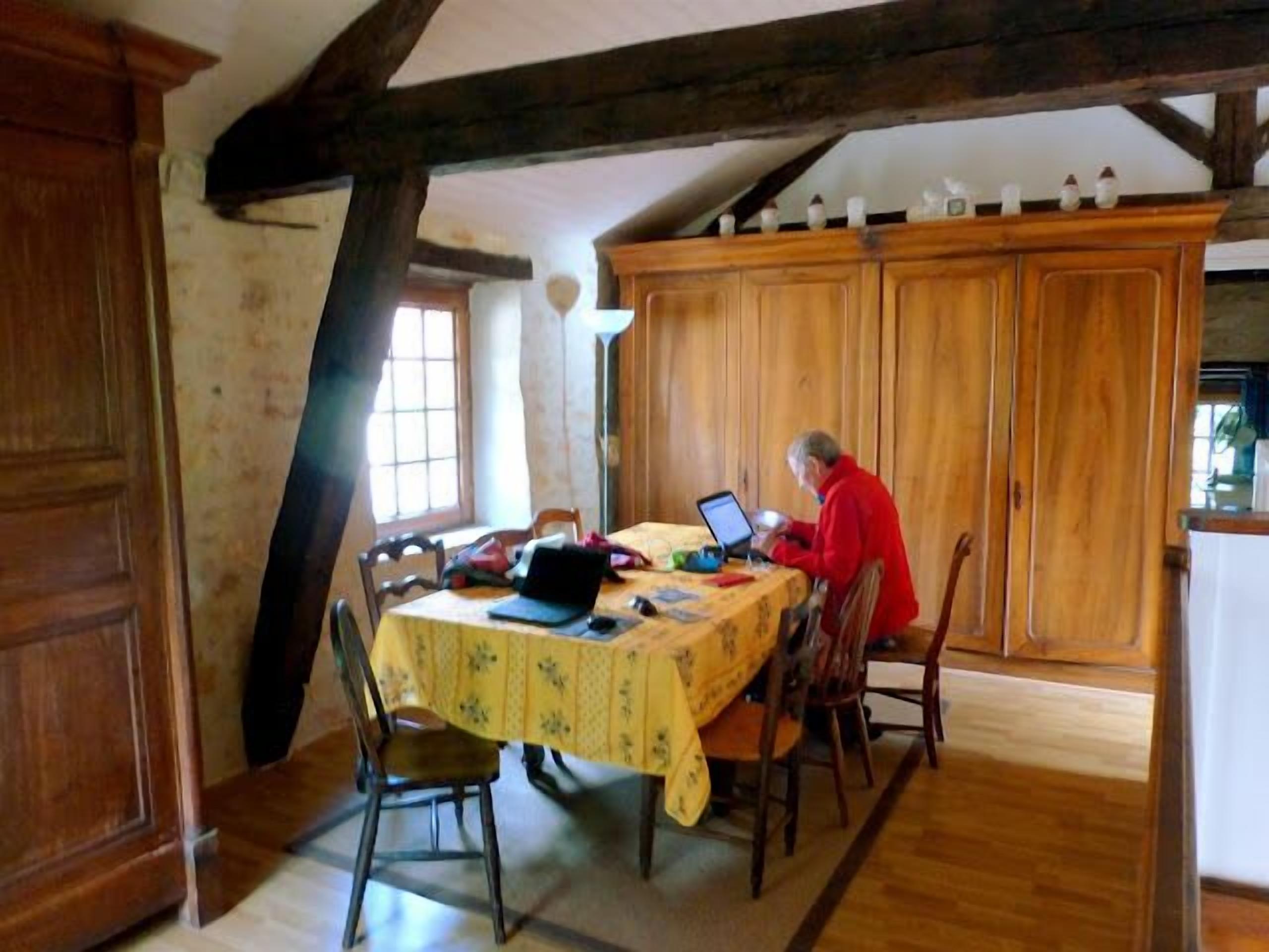 Ein Essbereich mit Holztisch, Stühlen und einer Person, die einen Laptop benutzt.