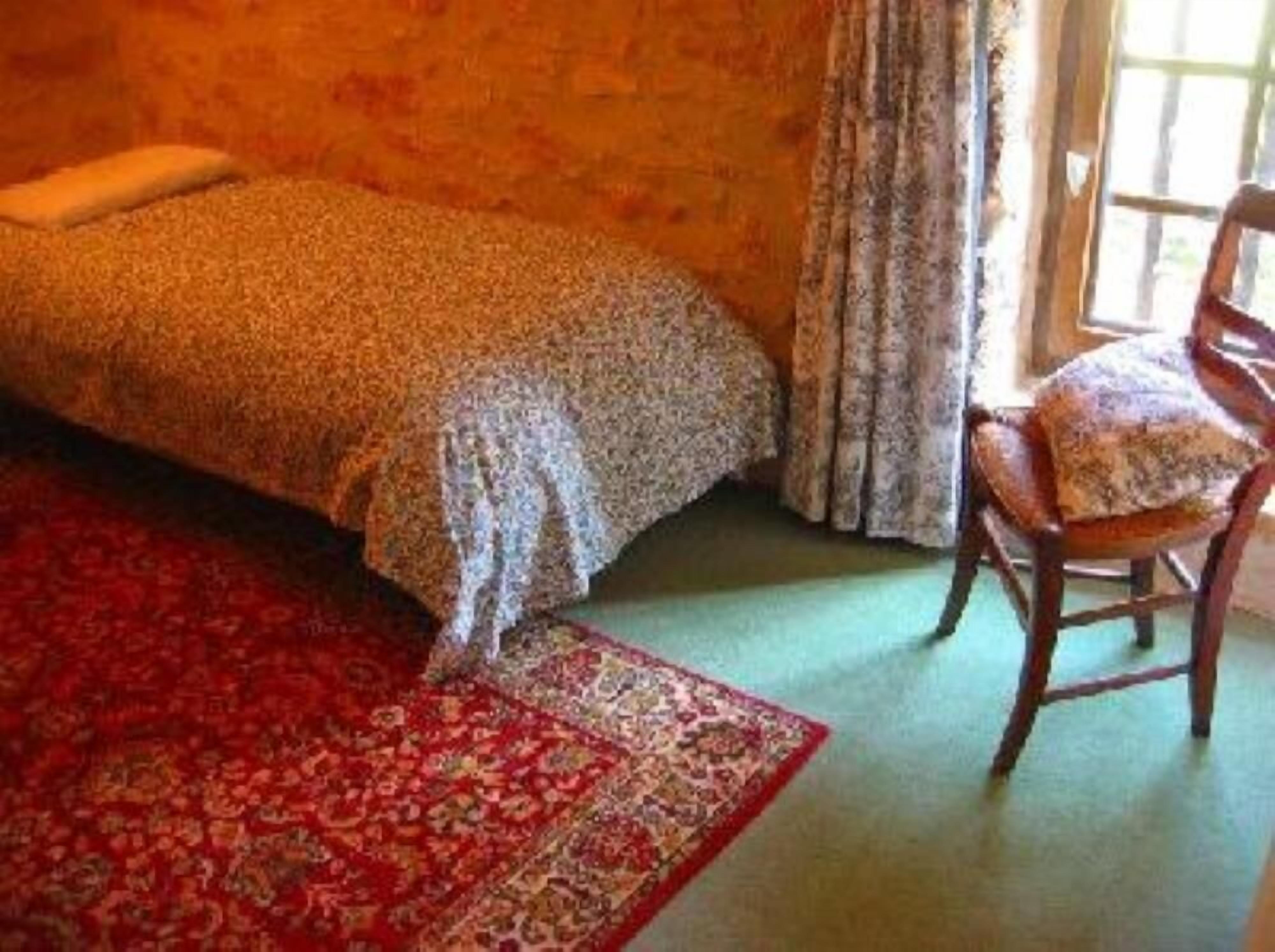 A room with a bed, a chair, a red carpet, and a window with curtains.