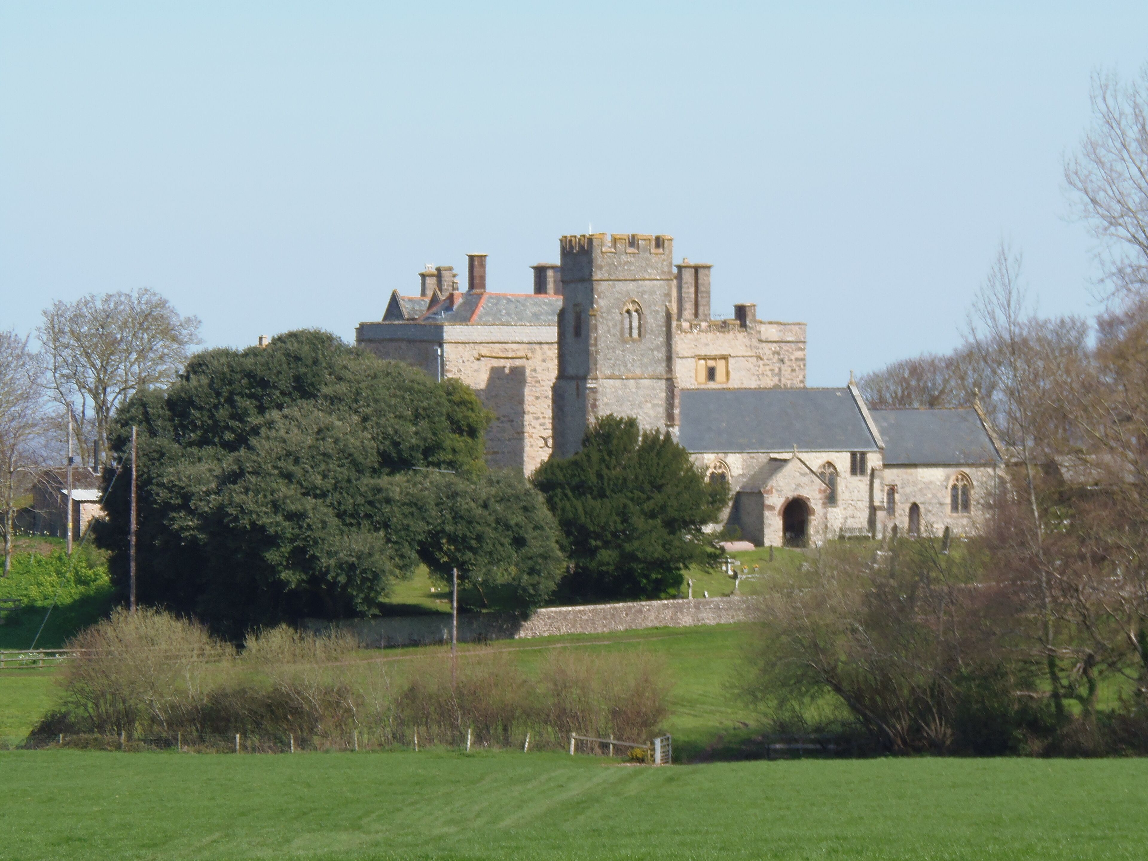 A historic stone building with a prominent tower, surrounded by lush greenery and a well-maintained lawn.