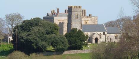 A historic stone building with a prominent tower, surrounded by lush greenery and a well-maintained lawn.