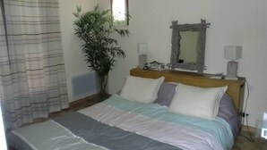 Ein Schlafzimmer mit einem Bett, einem Spiegel, einer Pflanze und einem Fenster mit Vorhängen.