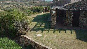 Een stenen huis met een stenen muur en een pergola, met uitzicht op een kustlandschap, zee en heuvels.