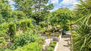 A lush garden with various plants and trees, a stone pathway, and a wooden bench. - Sea View Studio Flat with heated indoor pool & spa, countryside location (Hastings)
