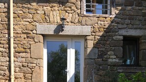 Un edificio de piedra con terraza de madera, una puerta blanca y plantas en macetas.