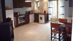 Cocina compacta con microondas, horno y lavadora, armarios de madera y un comedor con mesa y sillas.