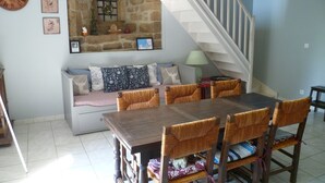 Un comedor con mesa de madera y sillas de mimbre, pared de piedra con ventana, y una escalera.