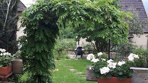 Een tuin met een houten boog bekleed met klimop, een geplaveid pad en potten met witte bloemen.