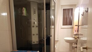 A compact bathroom with a glass-enclosed shower, a washing machine, a sink, and a toilet. - Big house near Appia Antica (Roma)