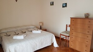 A neatly made bed with a white bedspread, a wooden dresser with multiple drawers, a chair, and a small table with a lamp. - Big house near Appia Antica (Roma)