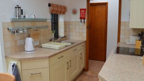 A kitchen with a sink, a kettle, and a coffee maker. There is a wooden door and a fire extinguisher on the wall.