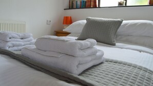 A neatly made bed with folded white towels, a grey quilted throw, and a bedside lamp.