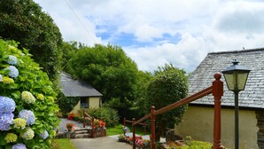 A stone staircase leading to a house with a thatched roof, surrounded by lush greenery and flowering plants.