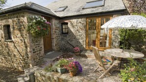 A stone house with a wooden door, a window, and a patio with a table and chairs.