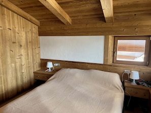 Une chambre dans un chalet en bois, avec un lit, deux tables de chevet et une fenêtre donnant sur un paysage agréable.