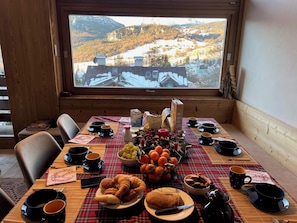 Une table à manger dressée avec de la nourriture et des boissons, et une vue sur un paysage enneigé par la fenêtre.