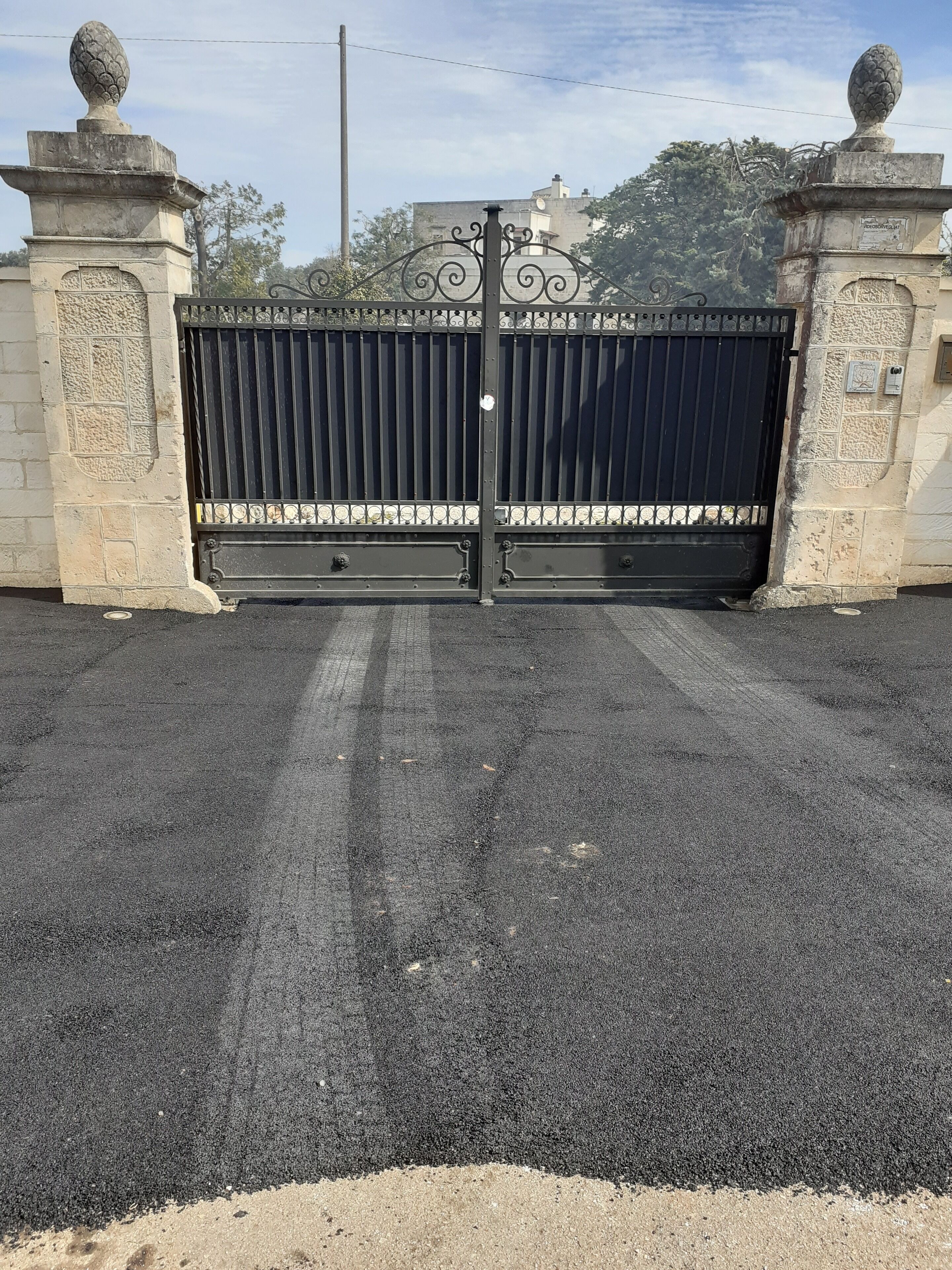 Een poort met een zwart metalen hek, stenen pilaren en decoratieve details.