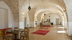 A spacious room with a high arched stone ceiling, a dining table with chairs, and a painting on the wall.