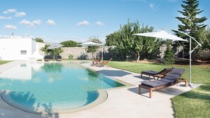 A modern outdoor pool area with lounge chairs and umbrellas, surrounded by a well-maintained lawn and trees.