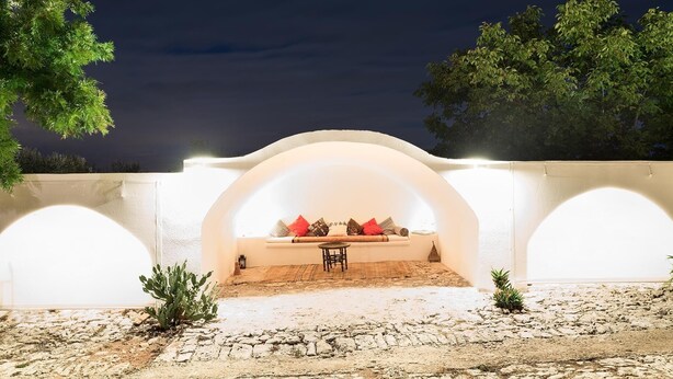 An outdoor seating area with a table and chairs, surrounded by white walls and arches, under a night sky.