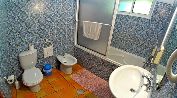 A bathroom with two toilets, a bidet, a sink, and a bathtub.